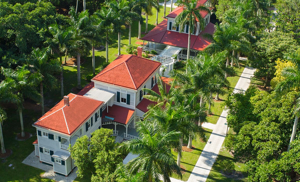 A bird 's eye view of a red roofed house surrounded by palm trees.