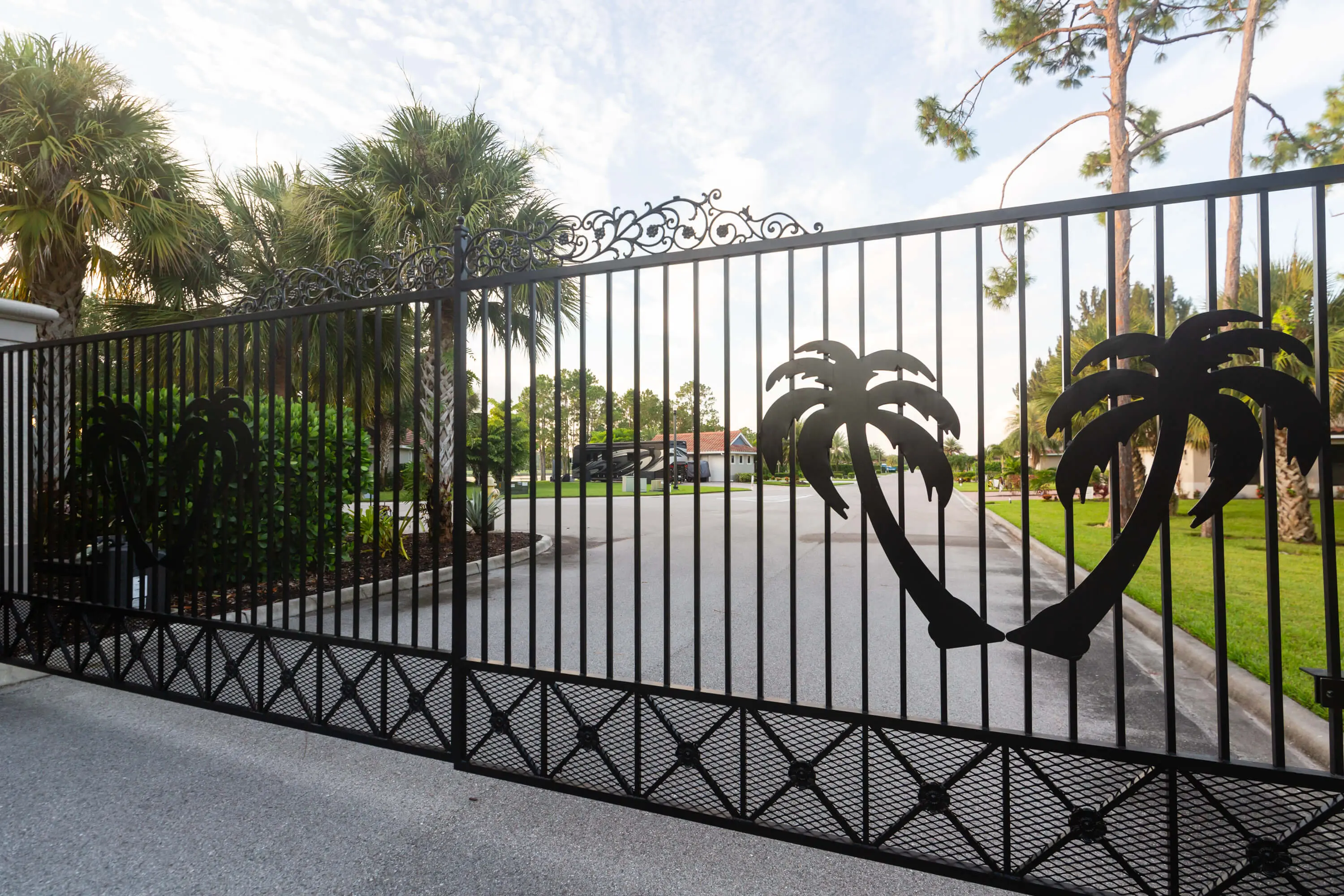 A gated driveway with palm trees and a fence.